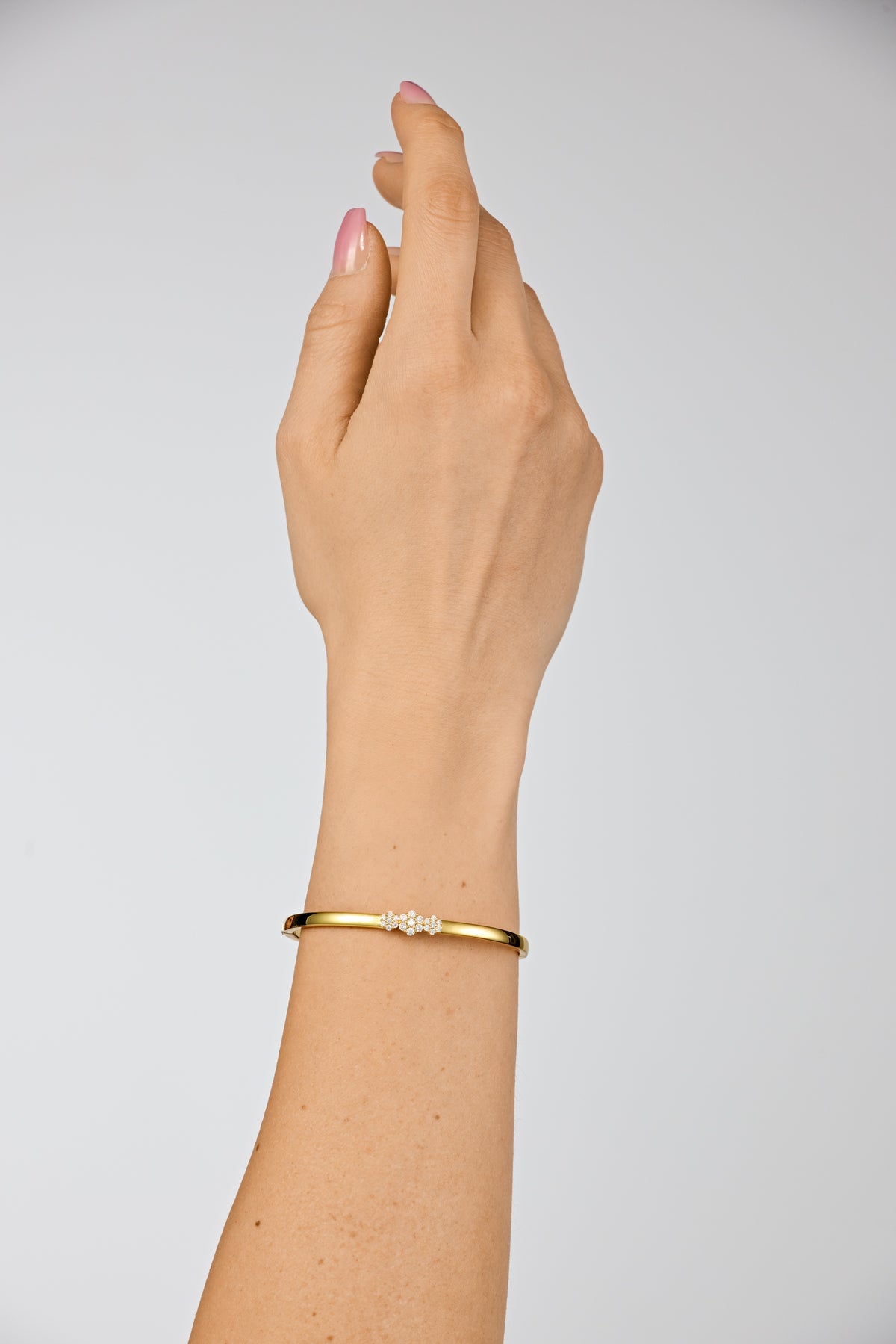 Model zeigt Armreifen der Marke Lunore mit Moissanit Edelsteinen der Klasse VVS1 in geschliffener Blumenform. Glänzender Silberarmreifen mit 18k Gelbgold Vergoldung